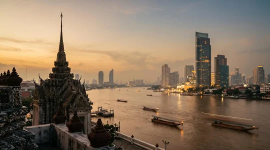 Vue panoramique de Bangkok au crépuscule mêlant toits de temples traditionnels et gratte-ciels modernes le long du fleuve Chao Phraya