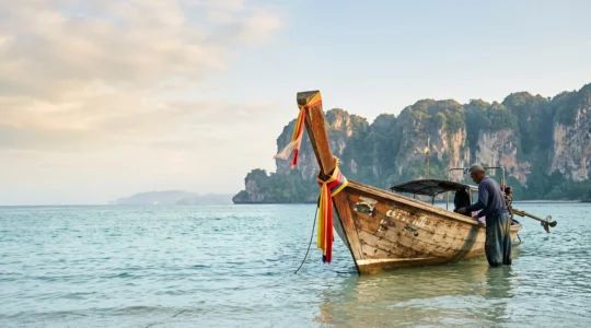 Longtail boat en bois amarré sur une eau turquoise face à des falaises calcaires en Thaïlande, prêt pour une location privée